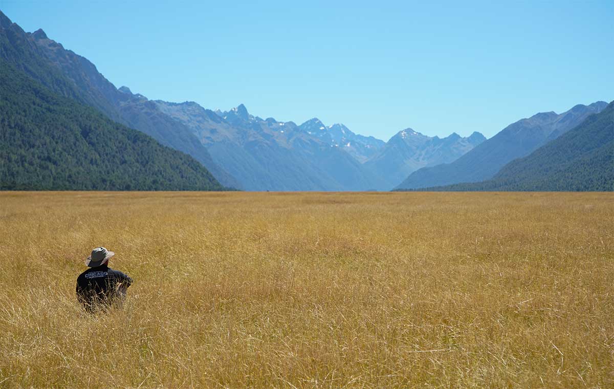 Man sits in grassy valley looking at mountains