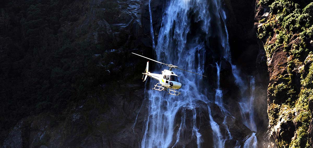 A helicopter flies across the front of a waterfall