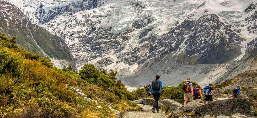 Hikers walking along New Zealand Great Walking trail with a glacier in the background